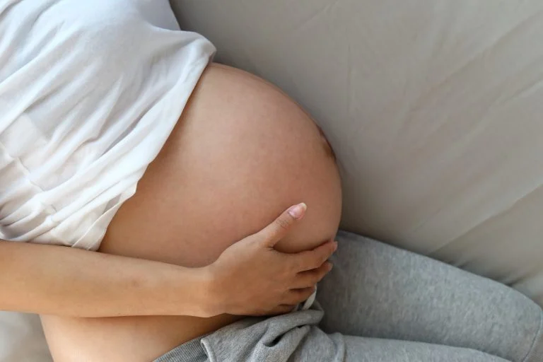 Mulher grávida deitada de lado. A foto está cortada na altura dos ombros
