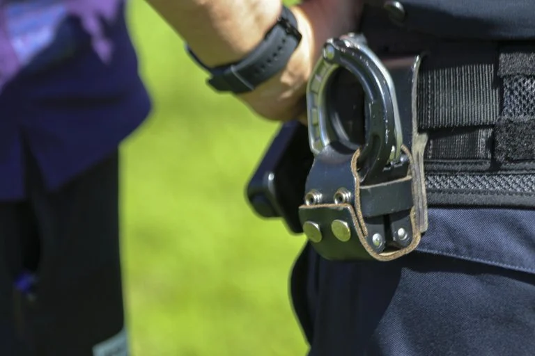 Policial com algema e arma na cintura