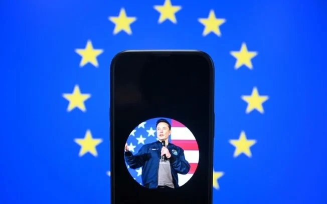 Um retrato do magnata Elon Musk, com uma bandeira da União Europeia ao fundo, em uma imagem tirada em Bruxelas em 7 de janeiro de 2025 Um retrato do magnata Elon Musk, com uma bandeira da União Europeia ao fundo, em uma imagem tirada em Bruxelas em 7 de janeiro de 2025