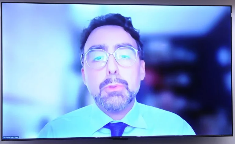 Homem participa de audiência remotamente, por meio de um telão