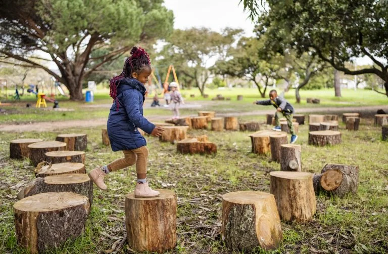 Menina feliz pulando em tocos de árvores no playground