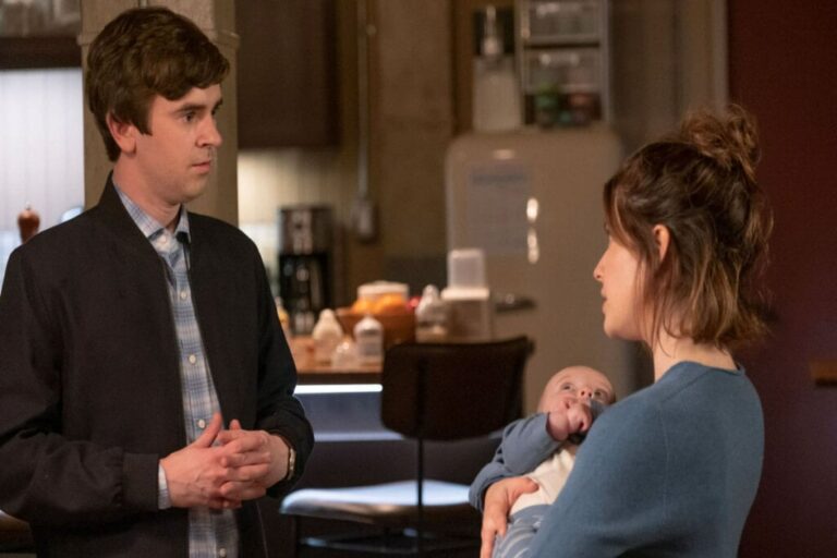 Um casal conversando de frente para o outro, o homem está de mãos cruzadas e a mulher segura um bebe