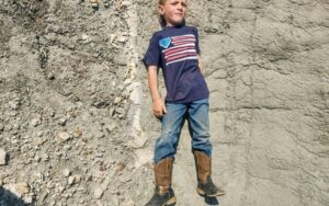 Liam Fisher deita-se ao lado do osso fossilizado de um dinossauro que ele encontrou em Badlands, na Dakota do Norte, em 2022