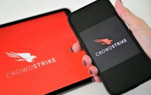 Mulher segura um telefone perto de um tablet que exibe o logotipo da empresa de segurança cibernética CrowdStrike, em 19 de julho de 2024, em Dubai, nos Emirados Árabes Unidos