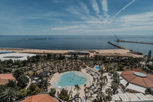Vista do alto mostra o hotel com uma piscina arredondada cercada de coqueiros, com o mar ao fundo