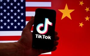 A logomarca do aplicativo de mídia social TikTok é exibida na tela de um iPhone, com um fundo das bandeiras dos EUA e da China, em Washington, DC, em 16 de março de 2023